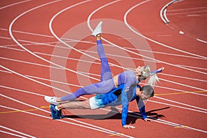 sport fitness couple training together stand in plank and do push up on outdoor stadium racetrack wearing sportswear