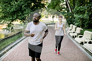 Sport fitness couple, young African man and Caucasian woman jogging outdoor in nature , at city park road. Two runners