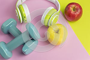 Sport fitness equipment with healthy food concept background.Two apples ,dumbbells and headphones on creative colorful background