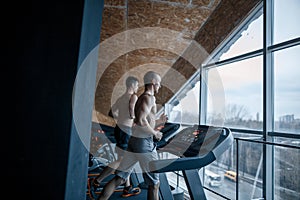 Sport, fitness, lifestyle, technology and people concept - close up of two men legs walking on treadmills in the gym.