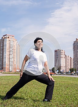 Smiling senior woman warming up stretching outdoors in the park