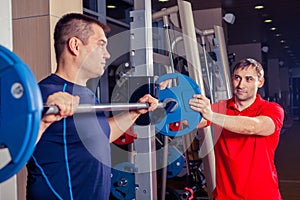 Sport, fitness, teamwork, bodybuilding people concept - man and personal trainer with barbell flexing muscles in gym