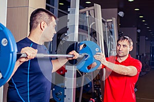 Sport, fitness, teamwork, bodybuilding people concept - man and personal trainer with barbell flexing muscles in gym