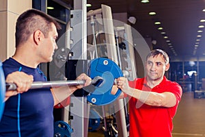 Sport, fitness, teamwork, bodybuilding people concept - man and personal trainer with barbell flexing muscles in gym