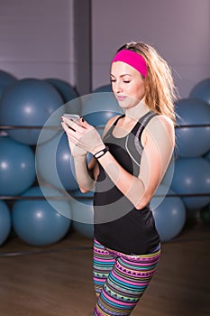 Sport, fitness, technology and people concept - young woman with activity tracker and smartphone in gym