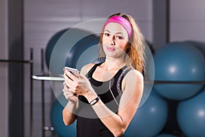 Sport, fitness, technology and people concept - young woman with activity tracker and smartphone in gym