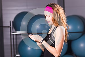 Sport, fitness, technology and people concept - young woman with activity tracker and smartphone in gym