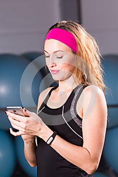 Sport, fitness, technology and people concept - young woman with activity tracker and smartphone in gym