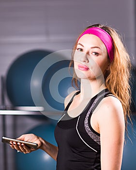 Sport, fitness, technology and people concept - young woman with smartphone in gym