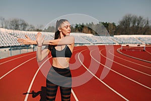 Sport fitness woman stretching on the stadium.Sport blond girl stretching arms in sport running arena with many tracks.