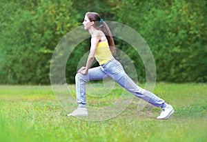 Sport, fitness and yoga concept - woman sportsman is doing stretching exercises on the grass