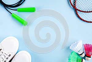 Sport flat lay with three multi-colored shuttlecocks, two rackets for playing badminton, jump rope and white sneakers on a blue