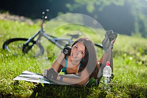 Sport girl lay on a grass with a map near the bicycle