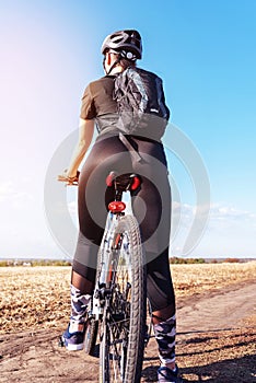 Sport girl on a mountain bike in the field rear view close up