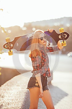 Sport happy girl posing in summer with skateboard. Stylish lucky hipster woman with colorful longboard in sunset in