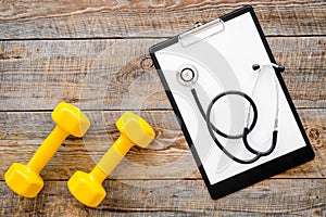 Sport and health. Fitness. Dumbbells and stethoscope on wooden background top view copyspace