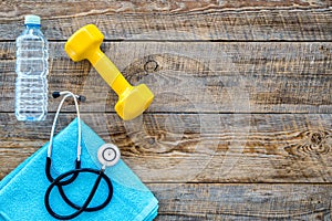 Sport and health. Fitness. Dumbbells and stethoscope on wooden background top view copyspace