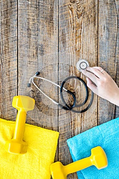 Sport and health. Fitness. Dumbbells and stethoscope on wooden background top view copyspace