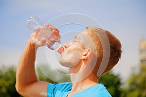 Sport, health and lifestyle concept. Portrait of young athletic man after training drinking water from bottle. Horizontal image