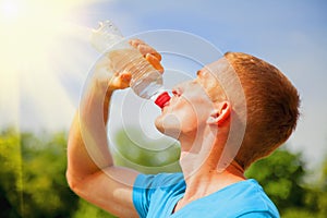 Sport, health and lifestyle concept. Young athletic man after training drinking water from bottle in sun rays