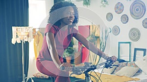 Sport at home, fitness at home concept. Cheerful african lady is using an exercycle to train in lockdown