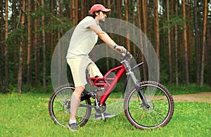 Sport, leisure and healthy lifestyle concept - young man sitting on a bicycle in the forest, male cyclist in profile on grass