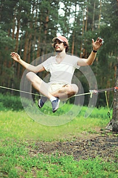 Sport, leisure, healthy lifestyle concept - young man slacklining balancing on a rope outdoors