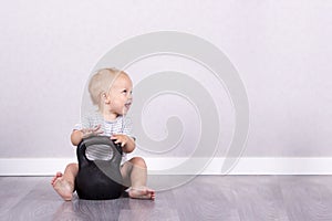 Sport is life. Happy laughing toddler sitting on the floor with kettlebell. Copy space