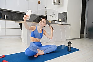Sport and lifestyle concept. Young woman doing workout at home on yoga mat, makes fitness vlog with smartphone, takes