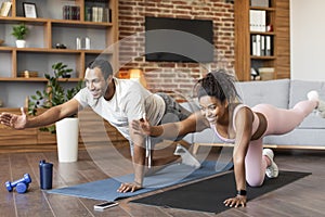 Sport lifestyle, family body care at home. Smiling young black guy and female in sportswear doing leg exercises