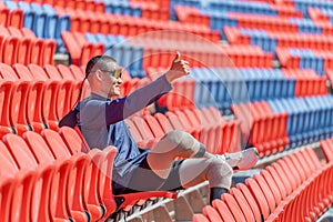 Sport man athlete prosthesis legs sit on chair of amphitheater look forward with show thumbs up in the stadium with day light