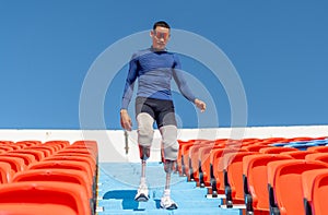 Sport man athlete prosthesis legs walk down on stairs of amphitheater in the stadium with day light