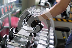 Sport man doing one-arm dumbbell rows of metal in modern gym.