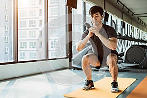 Sport man doing squat posture on yoga mat in fitness gym at condominium in urban. People lifestyles and Sport workout concept