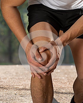 Sport man holding his knee in pain injured when running outdoors
