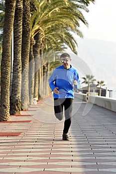 Sport man running along beach palm trees boulevard in morning jog training session