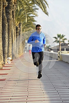 Sport man running along beach palm trees boulevard in morning jog training session