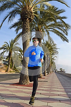 Sport man running along beach palm trees boulevard in morning jog training session