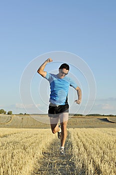 Sport man running outdoors on straw field doing victory sign in frontal perspective