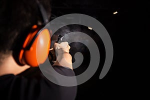 Sport man shooting pistol gun with smoke and fire bullet on black background in shootingrange