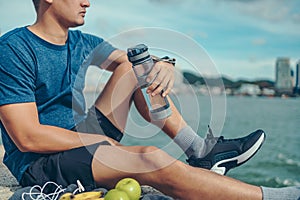 Sport man sitting after running and holding water bottle drink. Sport thirsty and resting after exercise
