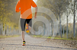 Sport man with strong calves muscle running outdoors in off road trail ground with trees under beautiful Autumn sunlight