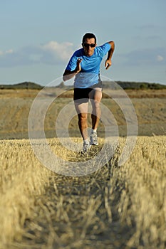 Sport man with sunglasses running outdoors on straw field ground in frontal perspective