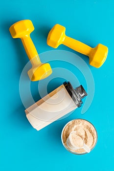 Sport nutrition. Whey protein, shaker, dumbbells on blue background top-down