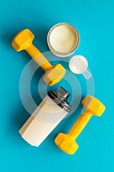Sport nutrition. Whey protein, shaker, dumbbells on blue background top-down flay lay