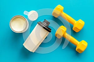 Sport nutrition. Whey protein, shaker, dumbbells on blue background top-down flay lay