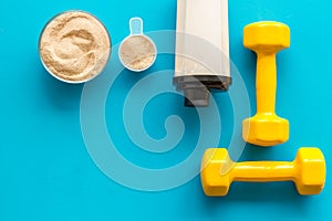 Sport nutrition. Whey protein, shaker, dumbbells on blue background top-down flay lay copy space