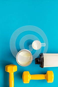 Sport nutrition. Whey protein, shaker, dumbbells on blue background top-down flay lay copy space