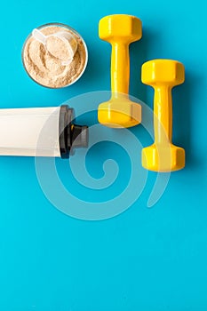 Sport nutrition. Whey protein, shaker, dumbbells on blue background top-down flay lay copy space