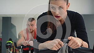 Sport people spinning pedals indoor bike at cycling class in gym club front view. Man and woman training bike exercise